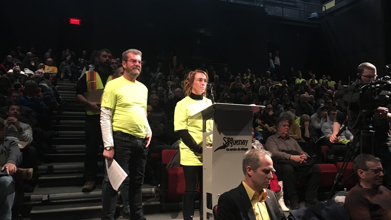 Un homme et une femme sont debout devant un lutrin. Ils attendent de poser une question à la mairesse.