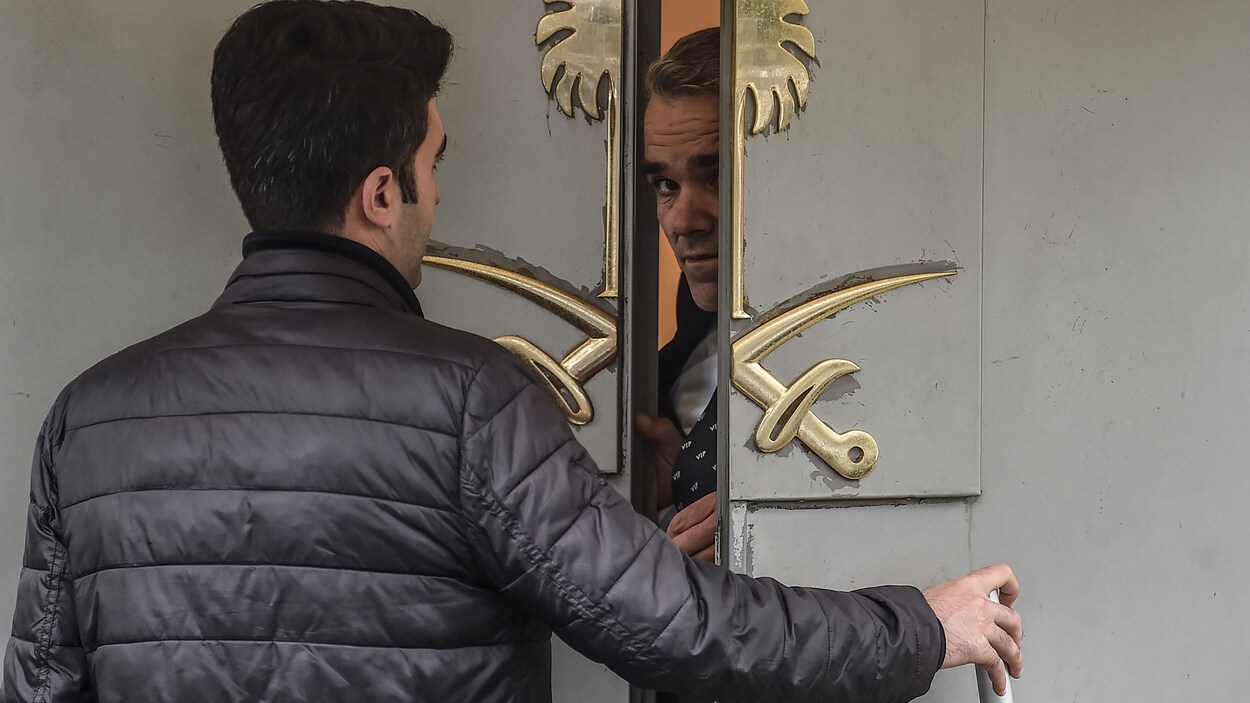 Le visage d'un responsable de la sécurité apparaît dans l'entrebâillement de la porte du consulat devant laquelle se trouve un homme