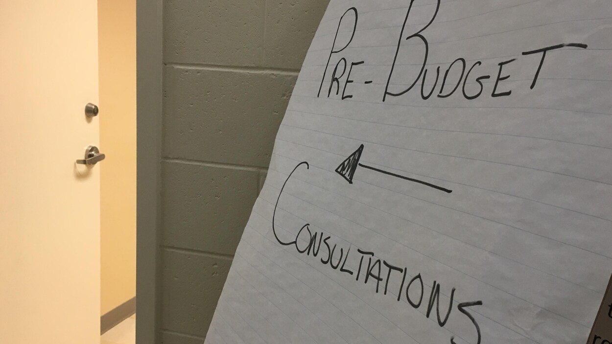 Une affiche indiquant une consultation prébudgétaire devant une porte entrouverte.