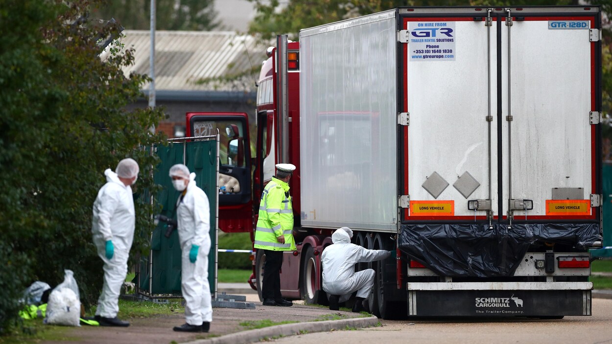 Quatre hommes équipés de combinaison s'affairent autour d'un conteneur.
