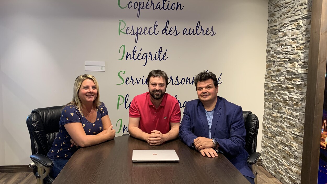 Une femme et deux hommes assis à une table sourient.