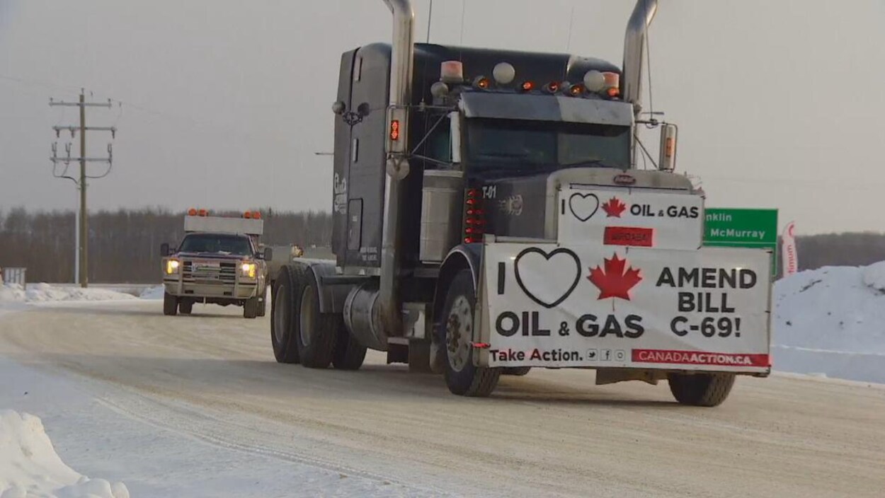 Un camion circule sur une route enneigée avec une bannière indiquant une opposition au projet de loi C-69.