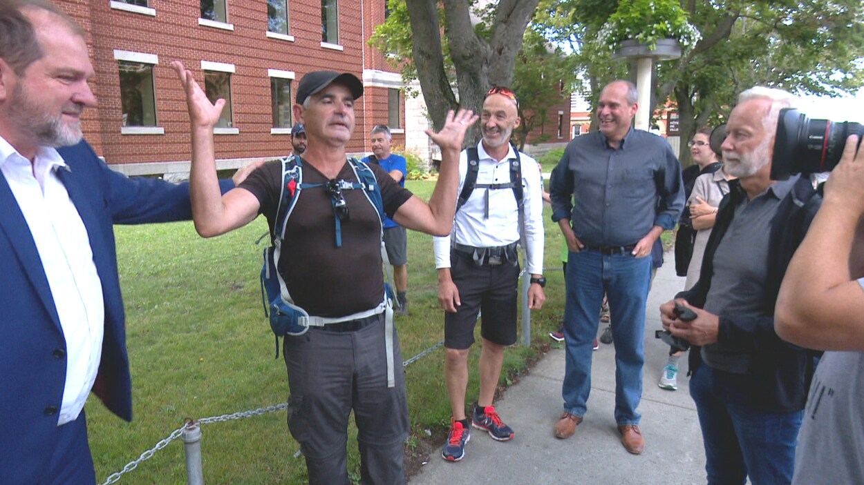 Le député Harold Lebel pose sa main sur l'épaule de Patrice Coquereau, pendant que le maire de Rimouski, Marc Parent, le député Guy Caron et des curieux regardent le comédien qui s'exprime devant une caméra.
