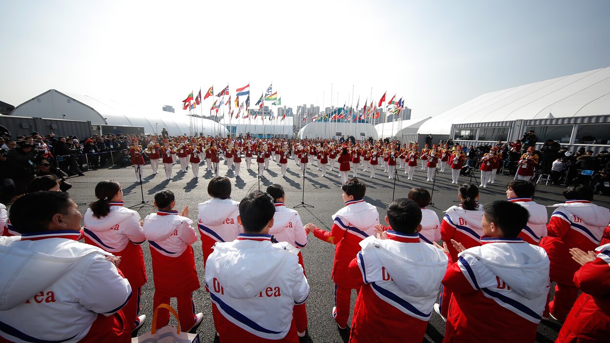Des athlètes nord-coréens regardent une fanfare jouer.