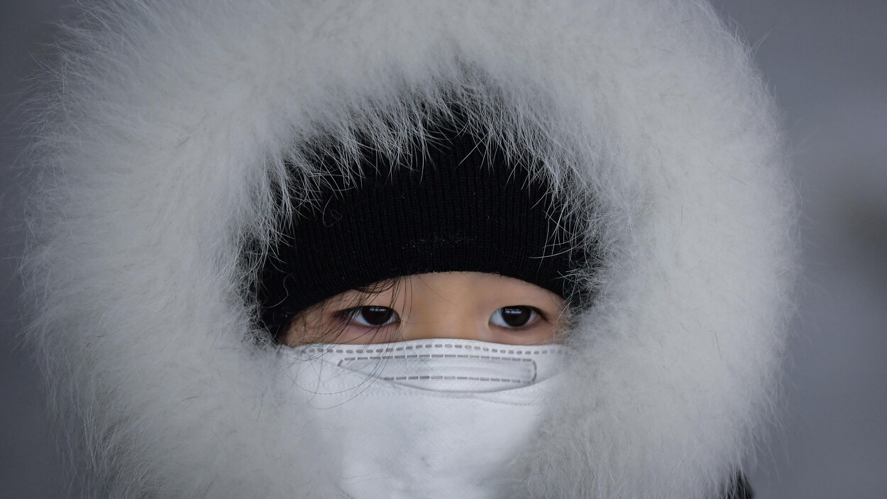 Un enfant la tête couverte d'un capuchon de fourrure et d'une tuque avec la bouche couverte d'un masque blanc assiste à une descente de luge à Pyeongchang, en Corée du Sud. Un enfant la tête couverte d'un capuchon de fourrure et d'une tuque avec la bouche couverte d'un masque blanc assiste à une descente de luge à Pyeongchang, en Corée du Sud.
