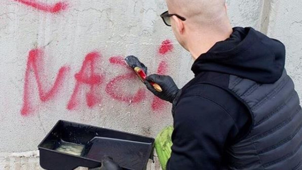 Un homme applique un produit liquide sur un graffiti antisémite afin de l'effacer.