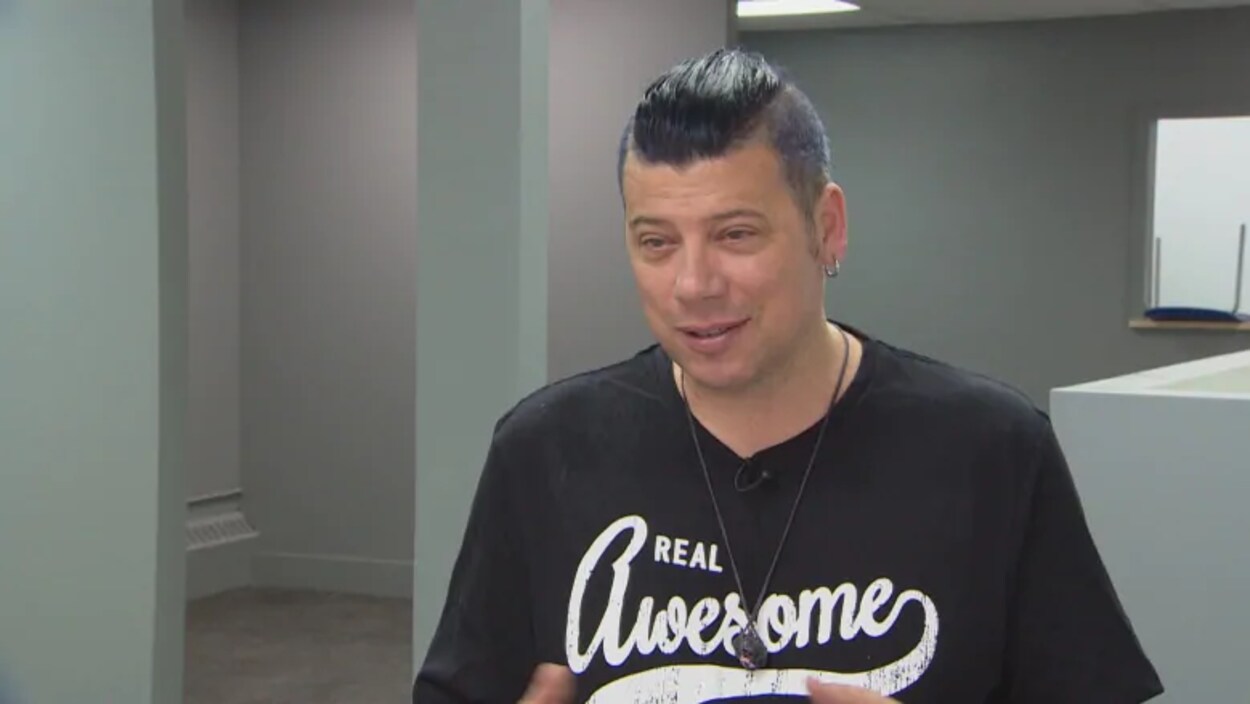 Un homme aux cheveux noirs, Corey Wyness, portant un chandail avec l'inscription Real Awsome.