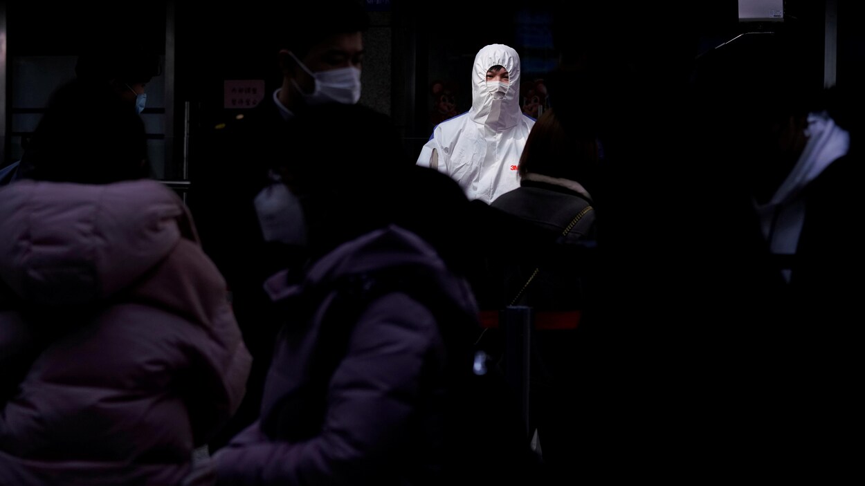 Une personne en uniforme blanc, dont seuls les yeux sont visibles, est au milieu d'autres personnes masquées.