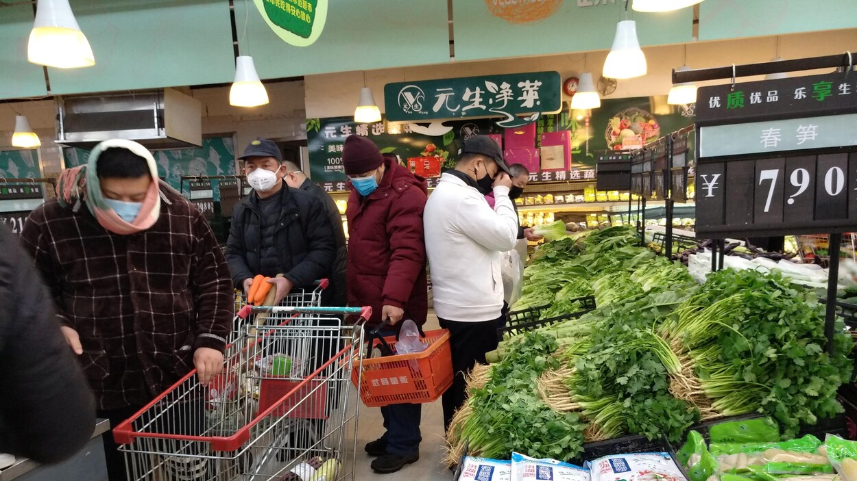 Des hommes portant des masques font la file pour passer à la caisse dans un marché.