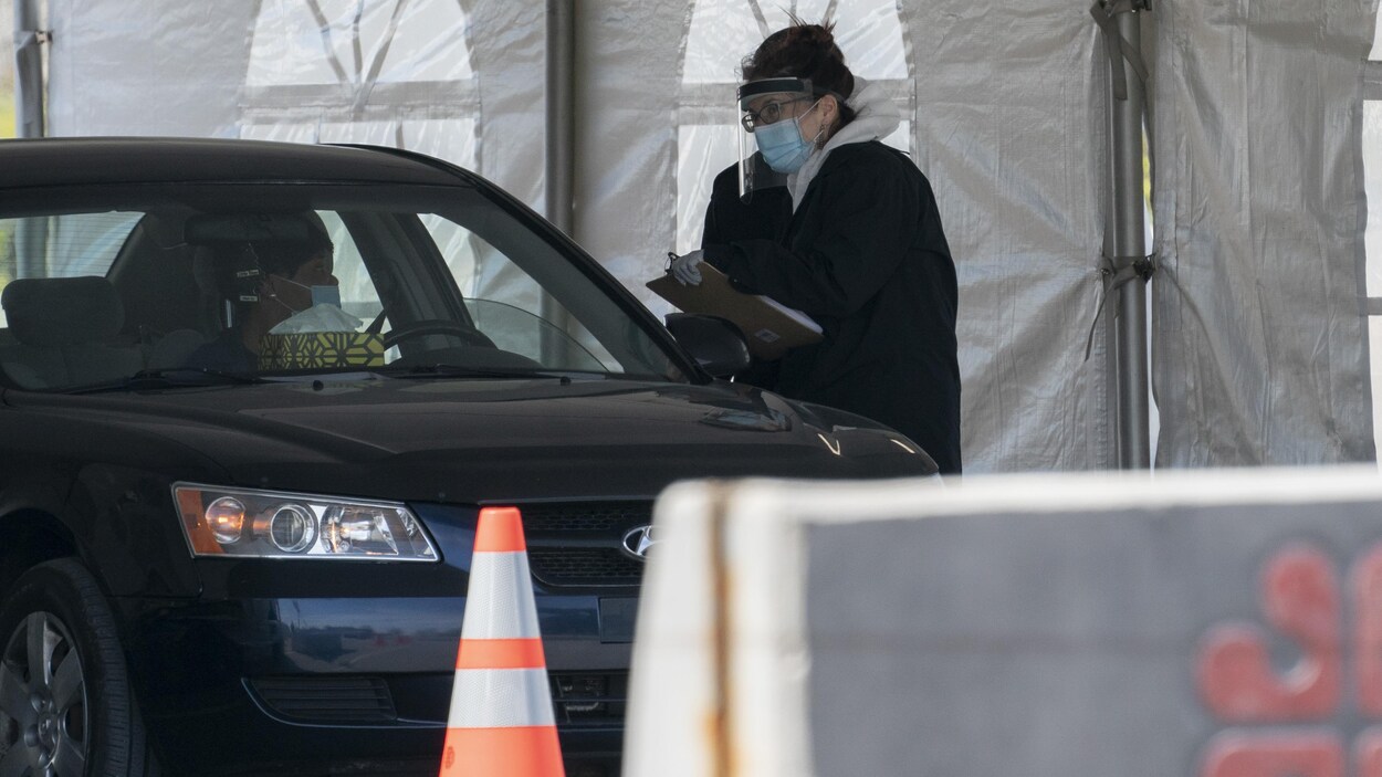 Une préposée de la santé fait passer un test de dépistage à quelqu'un qui est dans sa voiture.