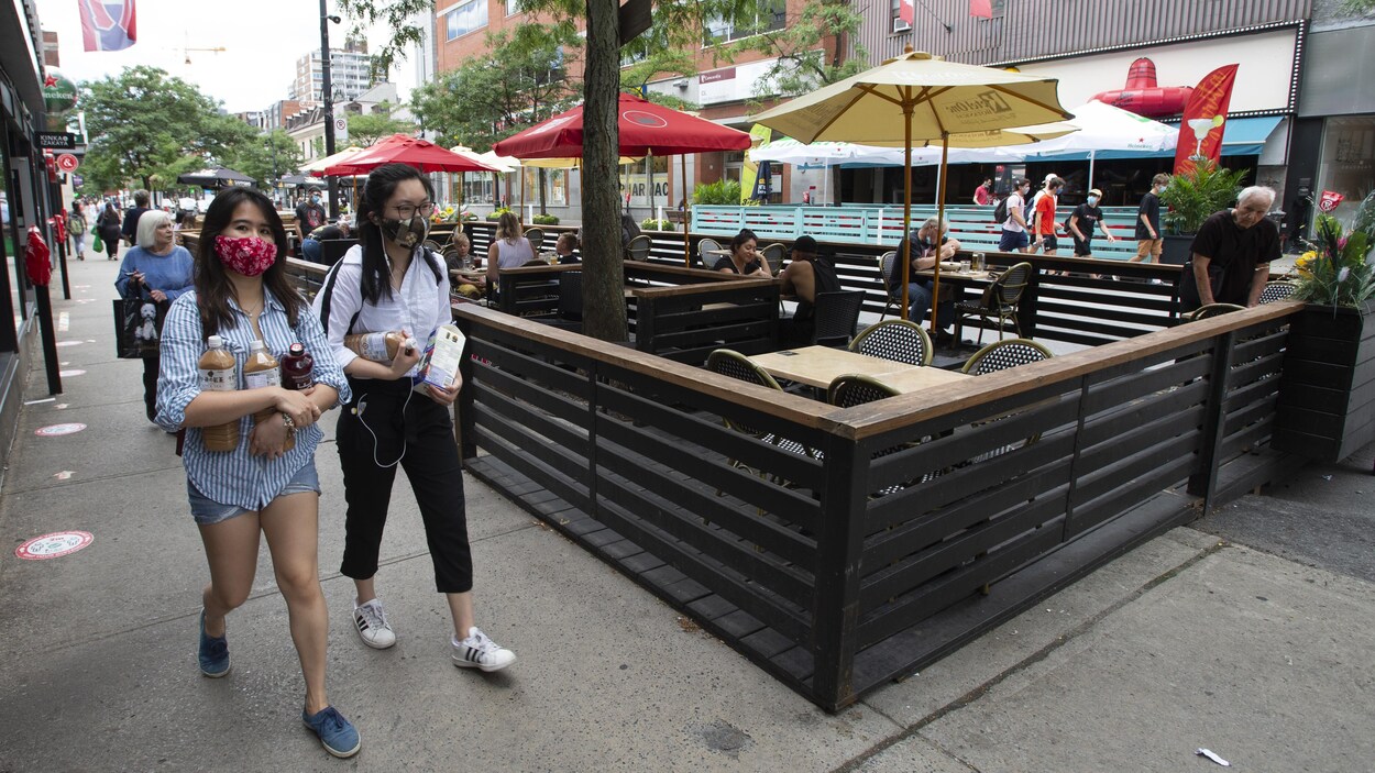 Des passant portant des masques marchent dans une rue de Montréal, près de la terrasse d'un restaurant.