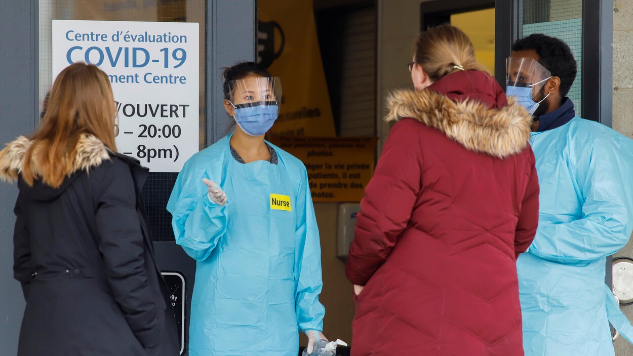 Deux infirmiers portant des gants, un masque et une jaquette parlent à deux femmes.