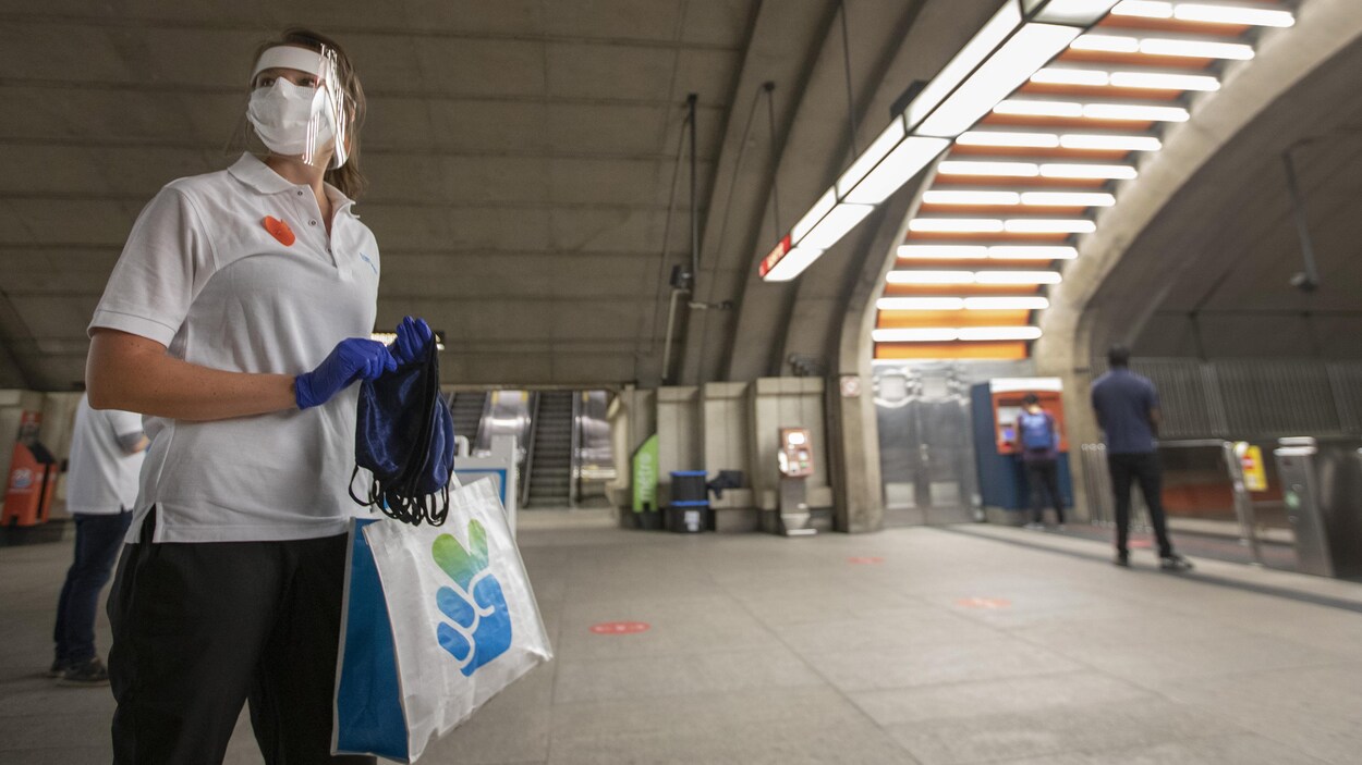 Une femme portant un masque et une visière distribue des masques dans une station de métro de Montréal.