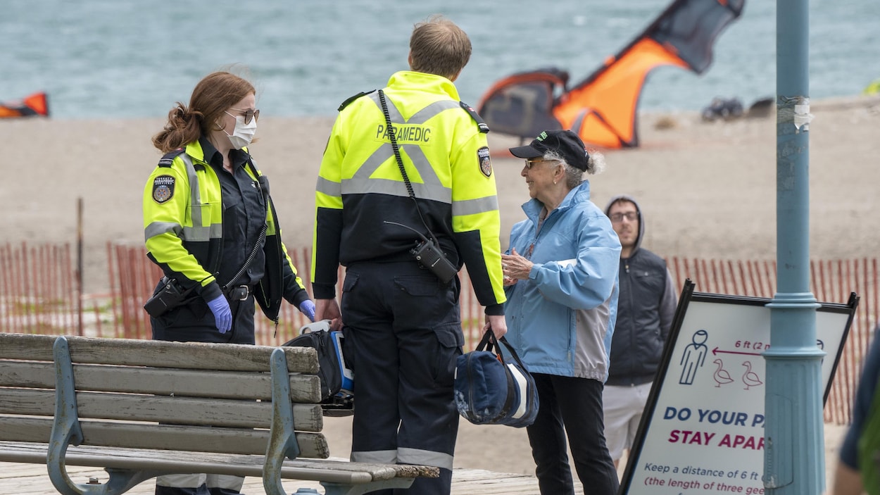 Des ambulanciers parlent avec une femme qui s'est assise sur un banc.