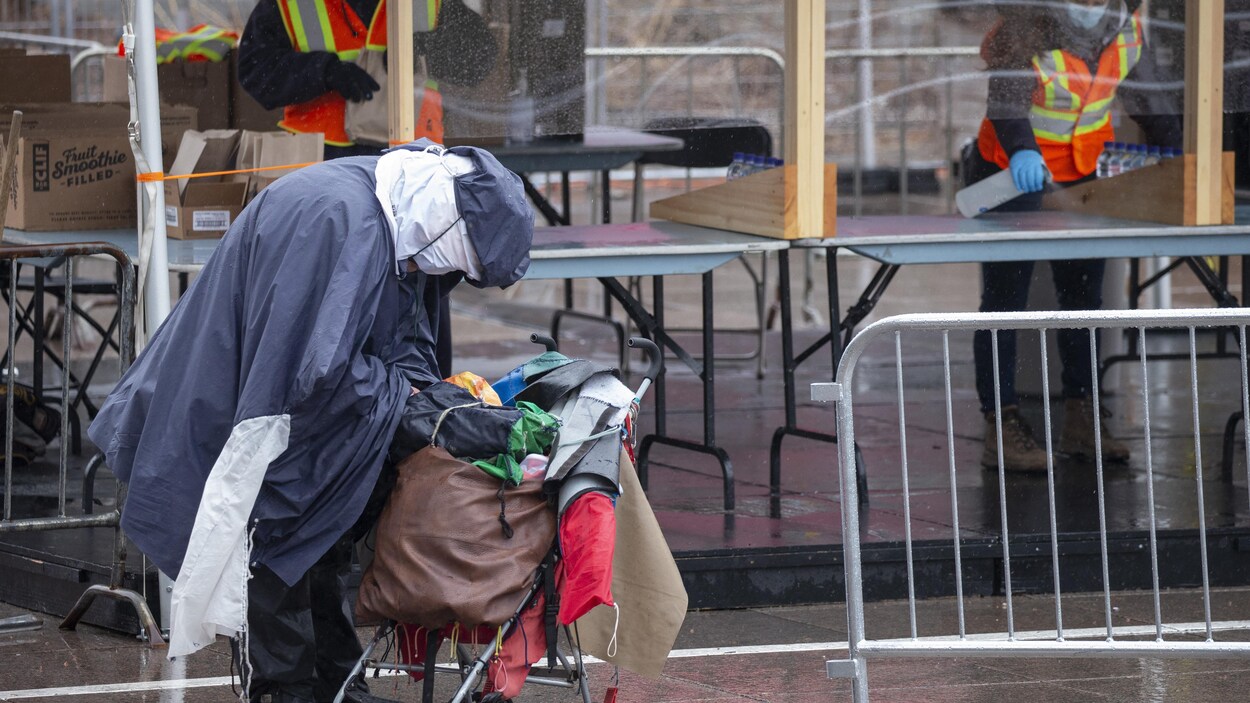 Une personne itinérante fouille dans ses sacs devant un comptoir de distribution d'aliments au centre-ville de Montréal.
