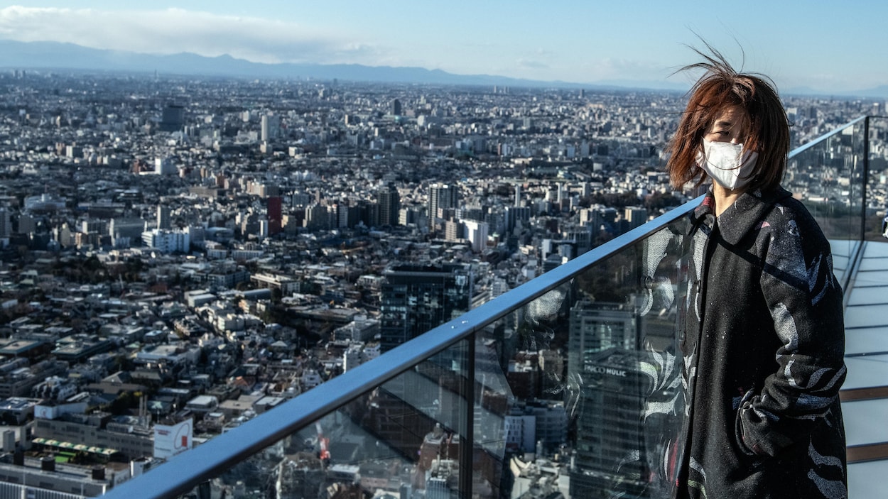 Une femme masquée surplombe Tokyo du haut d'une tour.