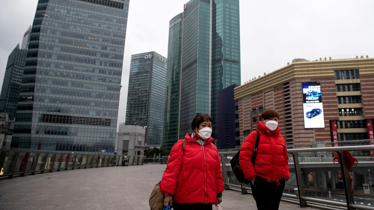 Deux femmes portant chacune un masque de protection marchent à l'extérieur, entourées de gratte-ciel.