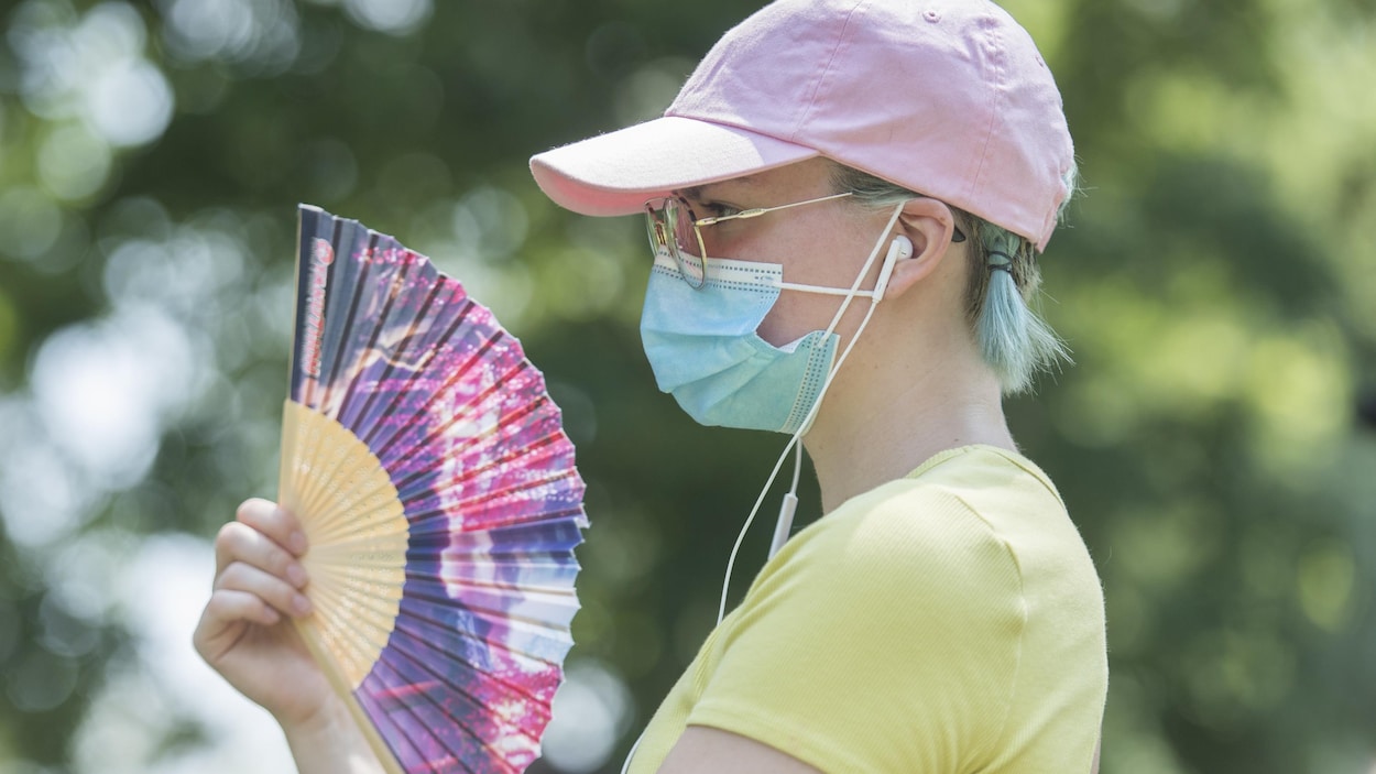 Une femme porte un masque dans un parc et se rafraîchit avec un éventail.