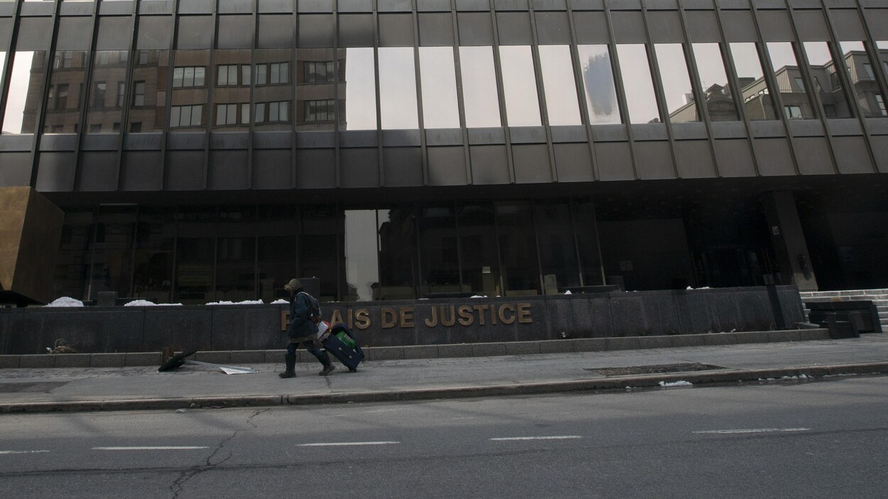 Un homme seul marche devant le palais de justice de Montréal en pleine journée.