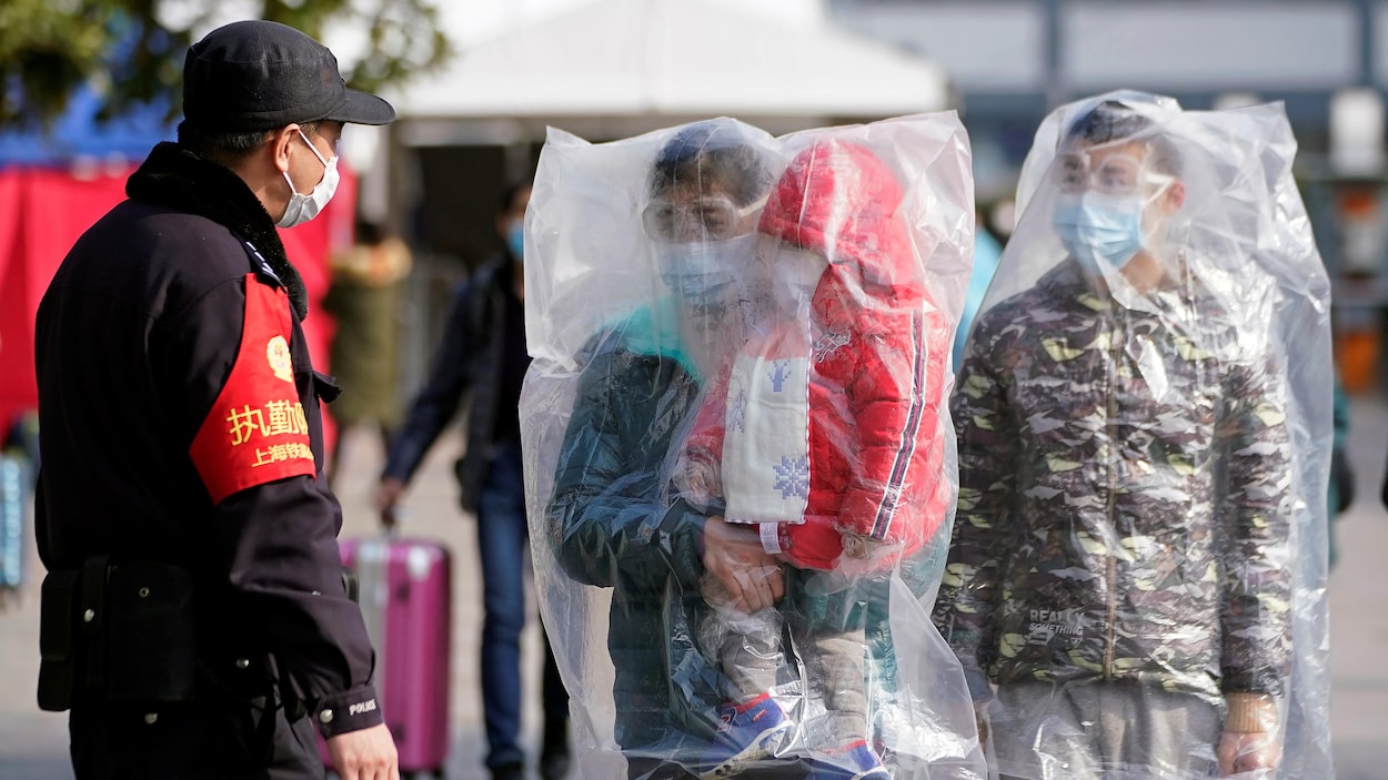 Un agent en uniforme et deux hommes, dont un porte un enfant, sont couverts de sacs en plastique.