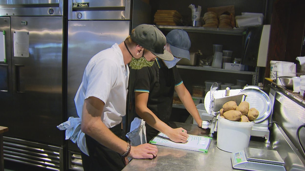 Deux employés d'un restaurant discutent dans la cuisine en portant chacun un masque.