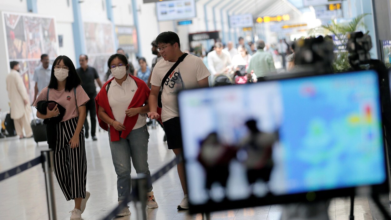 Des passagers portant un marque marchent dans un aéroport.