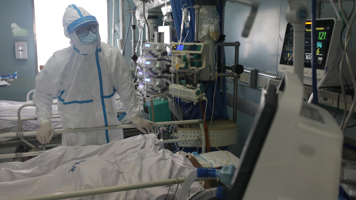 Un membre du personnel médical d'un hôpital habillé d'une combinaison de protection au chevet d'un malade.