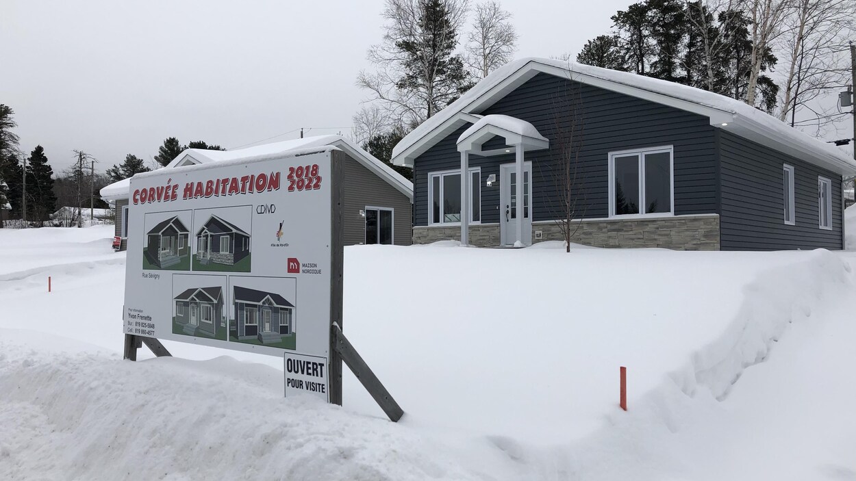 Une affiche indique Corvée habitation devant une petite maison, en hiver.