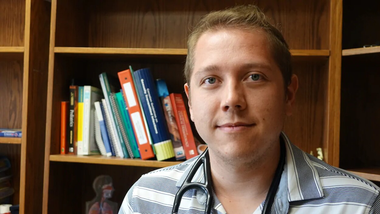 Le Dr Cory Scott pose pour la caméra dans un bureau de médecin.