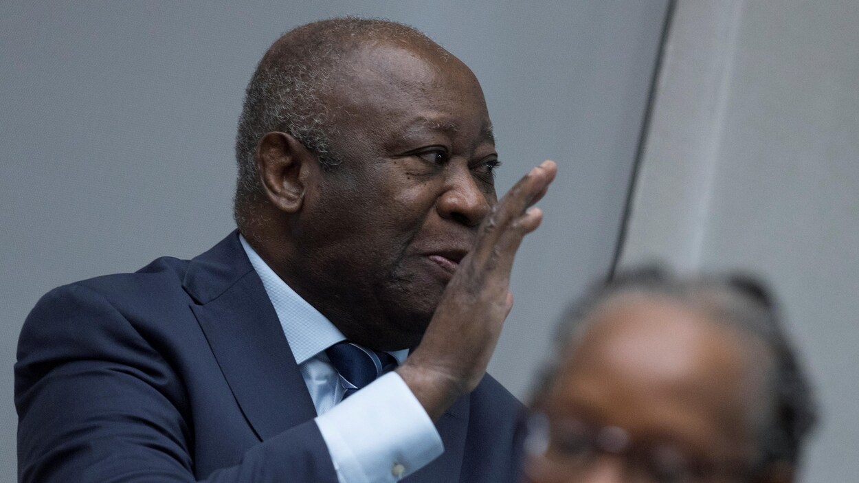 Un homme sourit en saluant de la main.