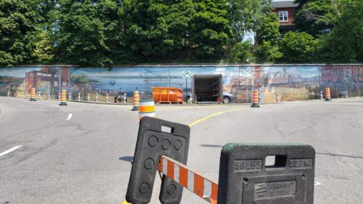 Une énorme murale sur un mur de béton dans la côte Plouffe à Trois-Rivières. En avant-plan, une barricade pour empêcher les gens d'y aller.