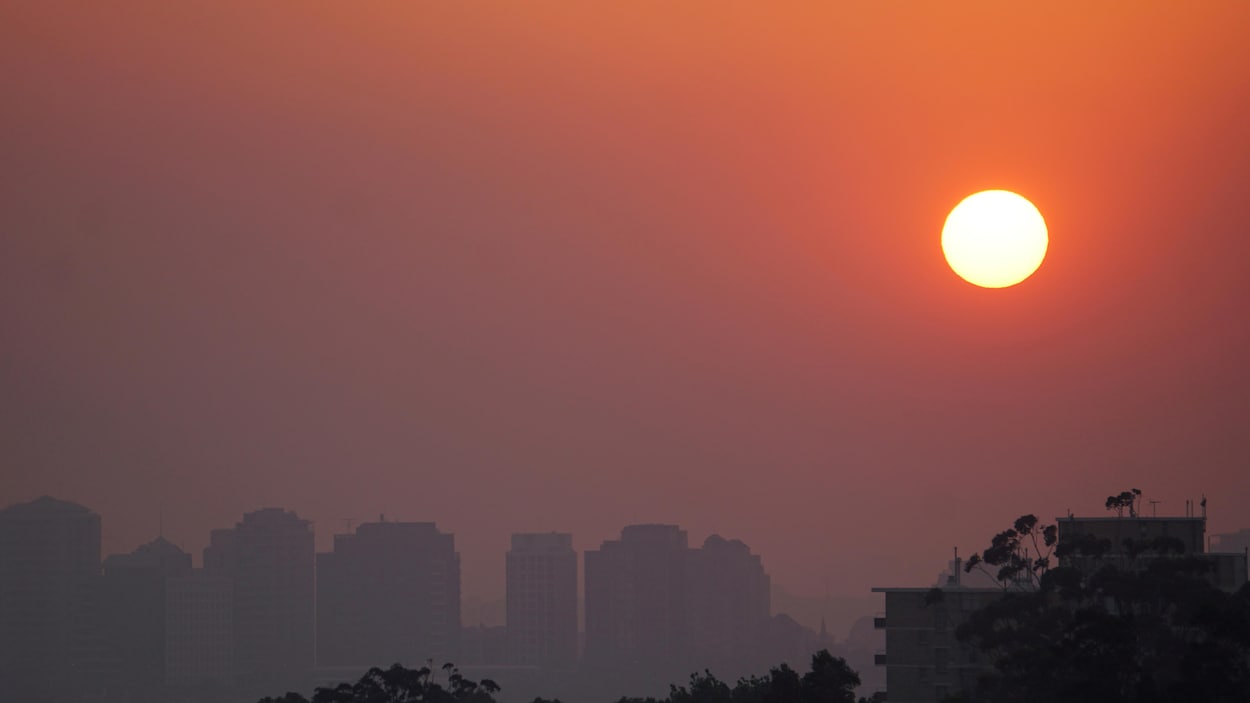 Un coucher de soleil avec un écran de fumée avec des immeubles en arrière plan. 