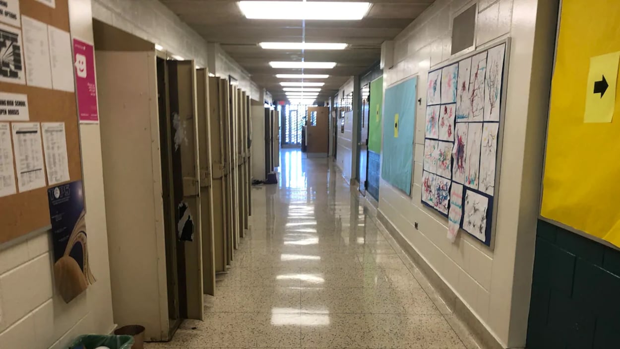 Un corridor vide dans une école. À gauche se trouvent des casiers et à droit des dessins sont affichés sur le mur.