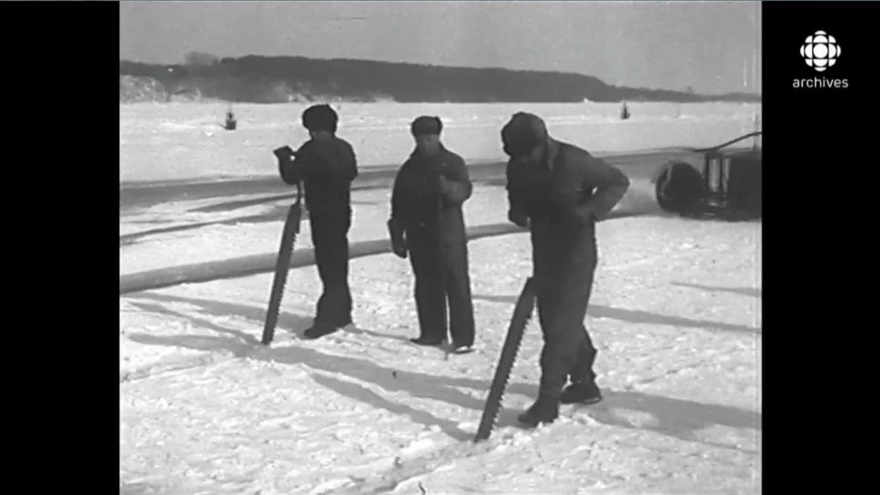 Deux coupeurs de glace équipés de longues scies taillant la surface de glace enneigée du fleuve. Un homme armé d'un long pic les accompagne.