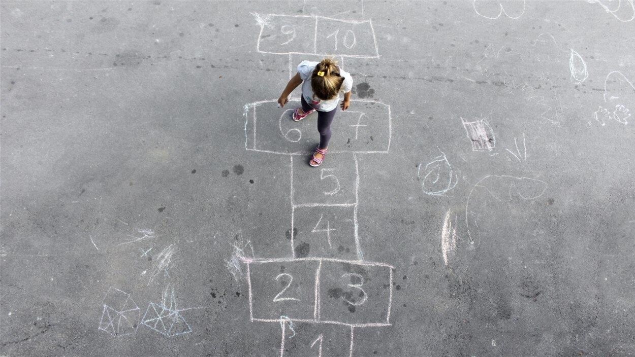 Une petite fille joue à la marelle dans une cour d'école