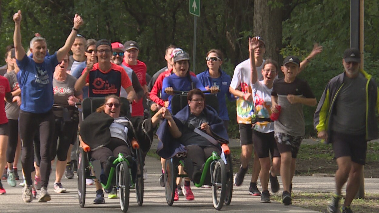 Deux femmes en fauteuil roulant se font poussées par des coureurs sur un sentier.