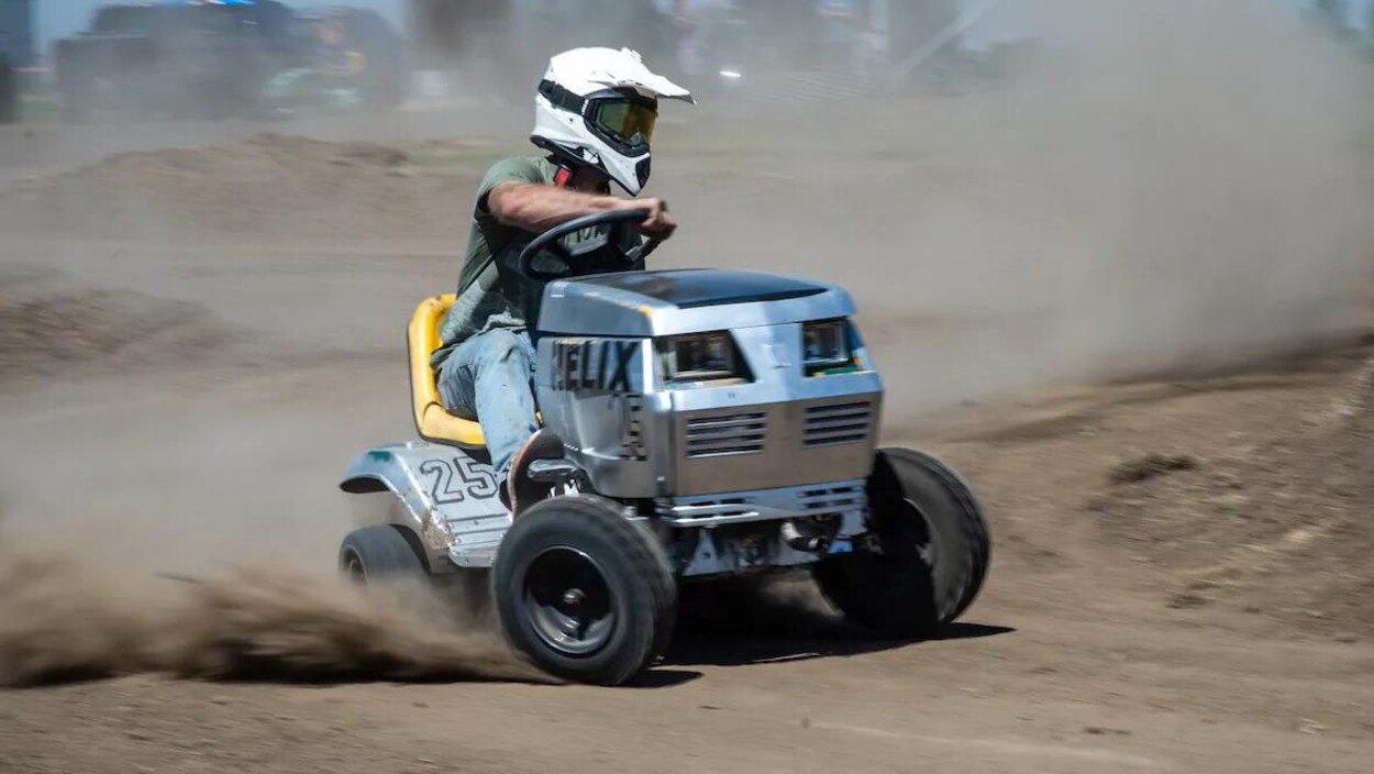Ue personne portant un casque conduit une tondeuse sur une piste de course en terre.