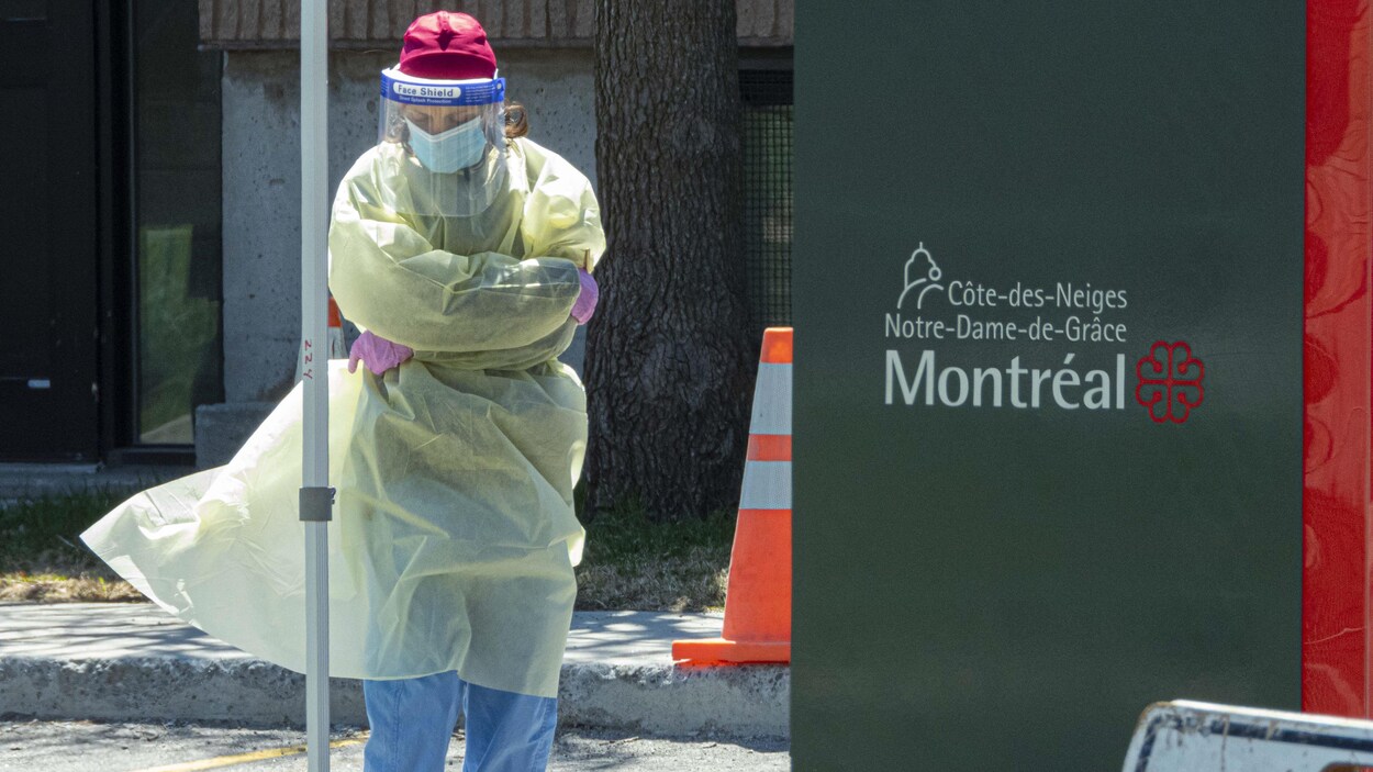 Une travailleuse de la santé, en équipement de protection, attend la tête baissée près de l'aréna.