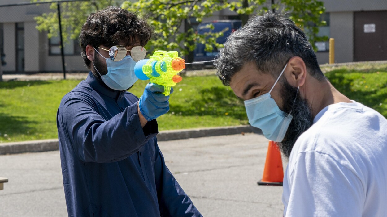 Un homme portant un masque en arrose un autre avec un pistolet à eau.