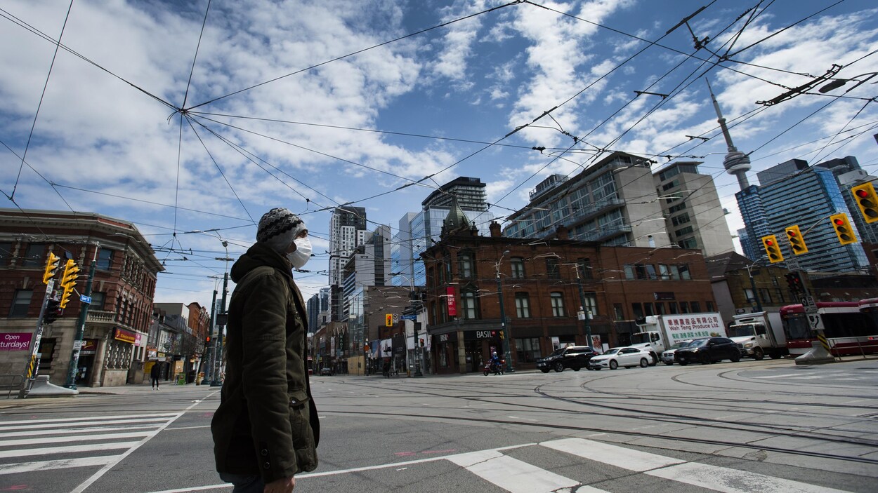 Un homme qui porte un masque traverse une rue de Toronto.