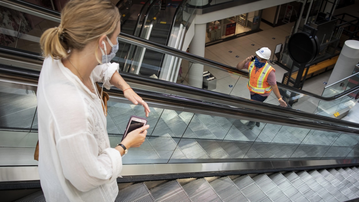 Une cliente et un ouvrier se croisent dans les escaliers roulants d'un centre commercial.