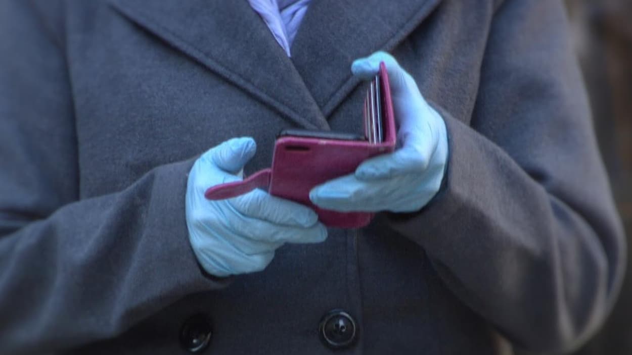 Une personne consulte son téléphone cellulaire avec des gants.