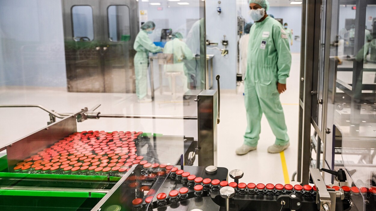 Un technicien habillé d'une combinaison et portant un masque observe une machine de loin.