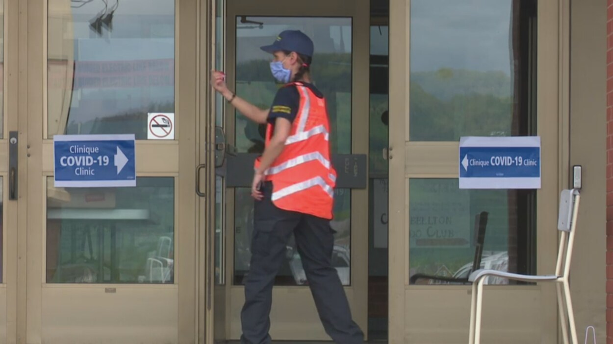 Une employé masqué entre dans un immeuble où l'on voit le signe de clinique COVID-19.