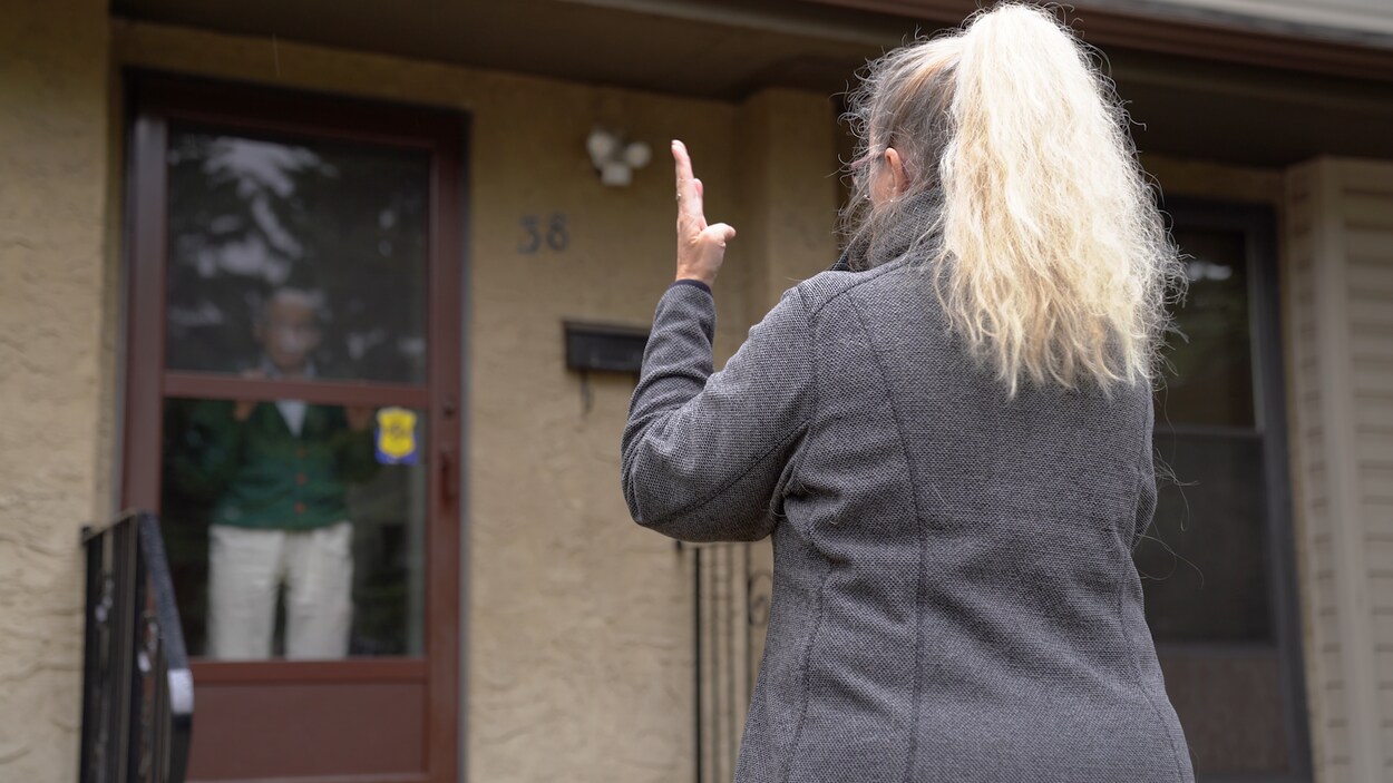 Un ainé discute avec une bénévole derrière sa fenêtre.