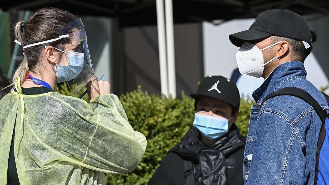 Une travailleuse de la santé portant masque et visière pose des questions à des clients à un centre de dépistage.