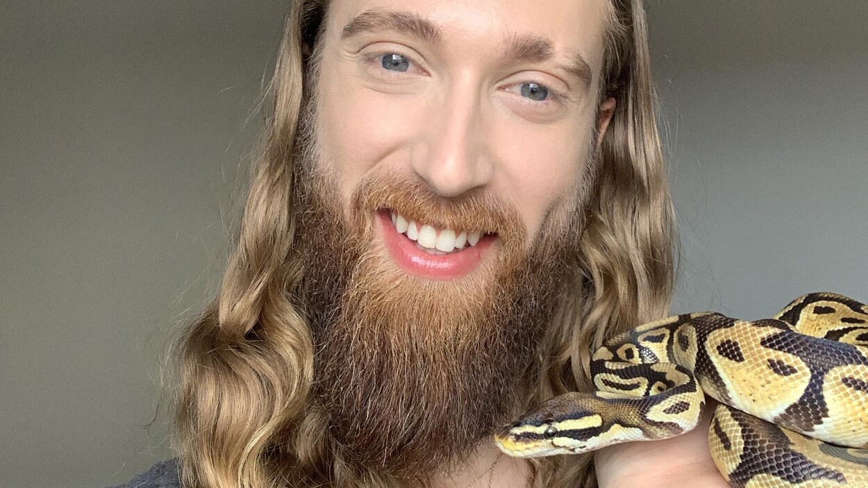 Un homme tient un serpent dans sa main à la hauteur de son visage.