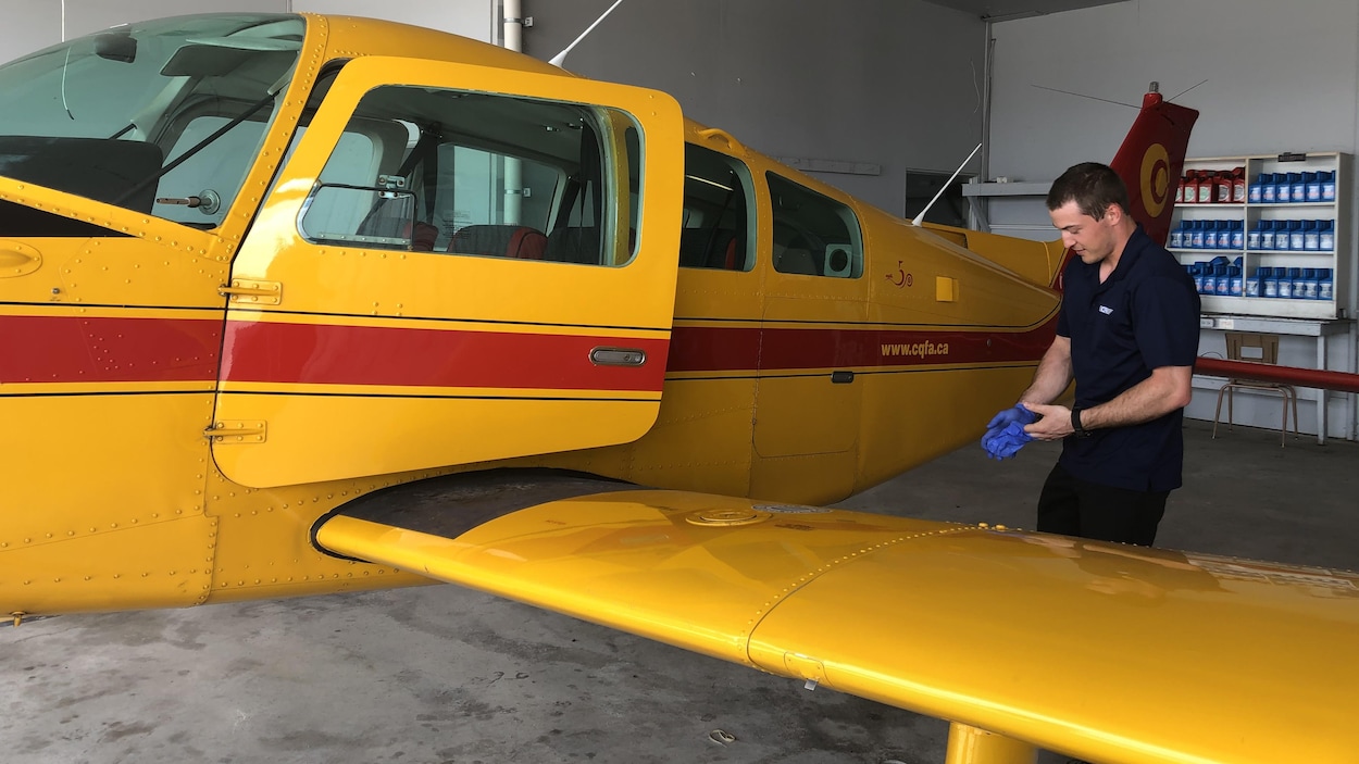 Un étudiant qui porte des gants, debout, à côté d'un avion de brousse.
