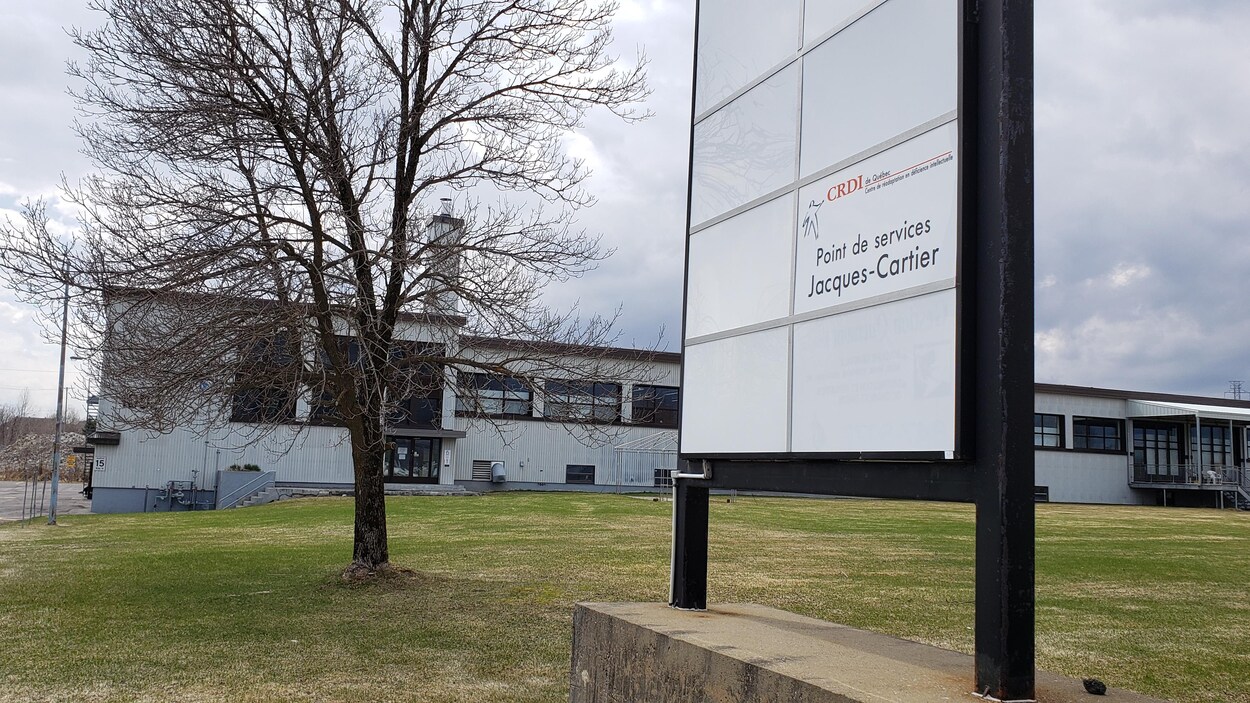 Une affiche sur laquelle on peut lire CRDI de Québec, point de services Jacques-Cartier. Un bâitment gris à l'arrière. C'est le jour, le printemps.