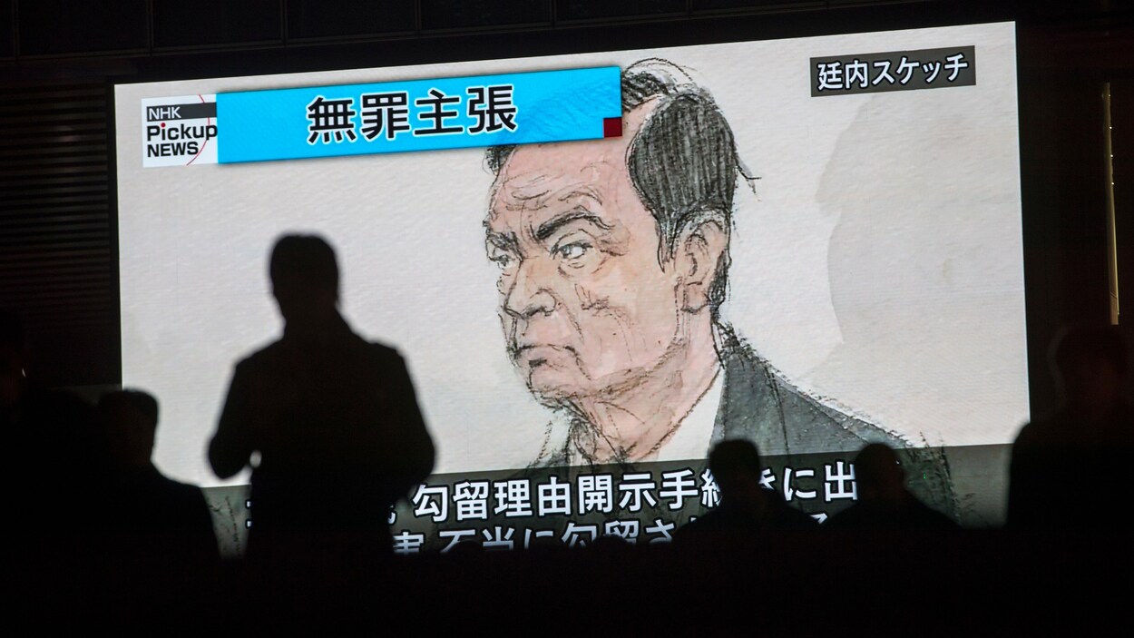Des passants devant un écran télé sur lequel on peut voir une caricature de Carlos Ghosn lors de son audition par la justice japonaise.
